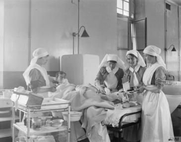 Female nurses dressing the wounds of a convalescent patient wounded at Zeebrugge at the Royal Naval Hospital, Chatham. © IWM (Q 18927)